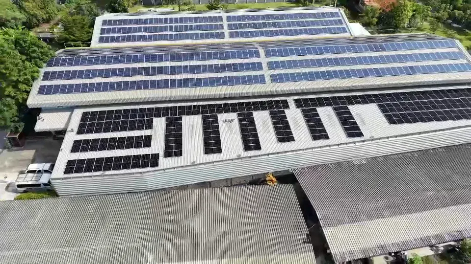 An aerial view of the plant, its roof covered in rows of solar panels, surrounded by greenery and a pond.