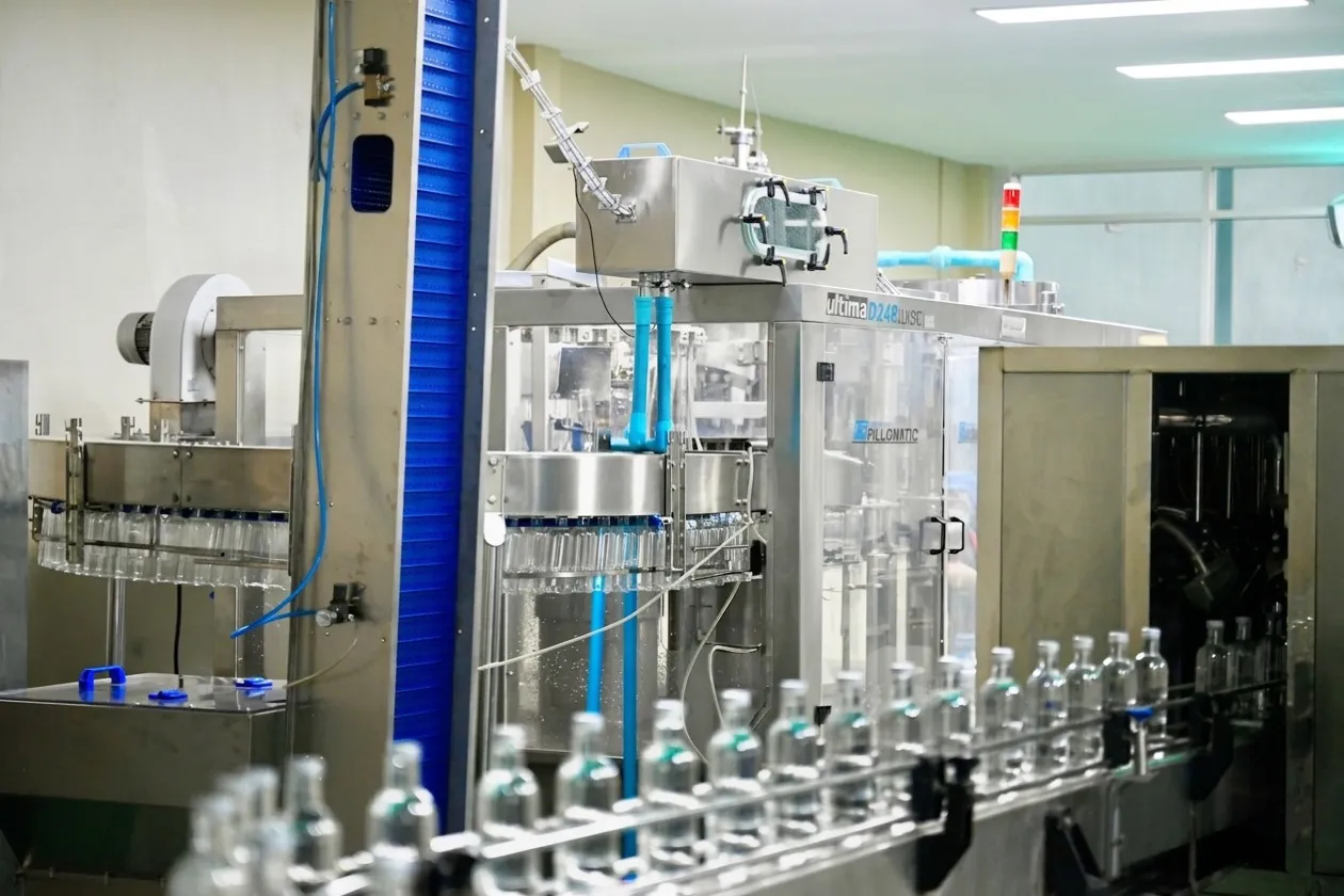 A rotary filling machine with clear bottles running out of it along a conveyor.